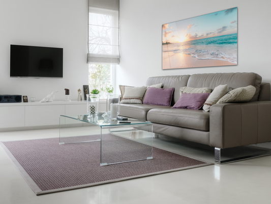 Beach wall art on top of a grey couch with pillows, a table, a rug and a tv on the next wall.