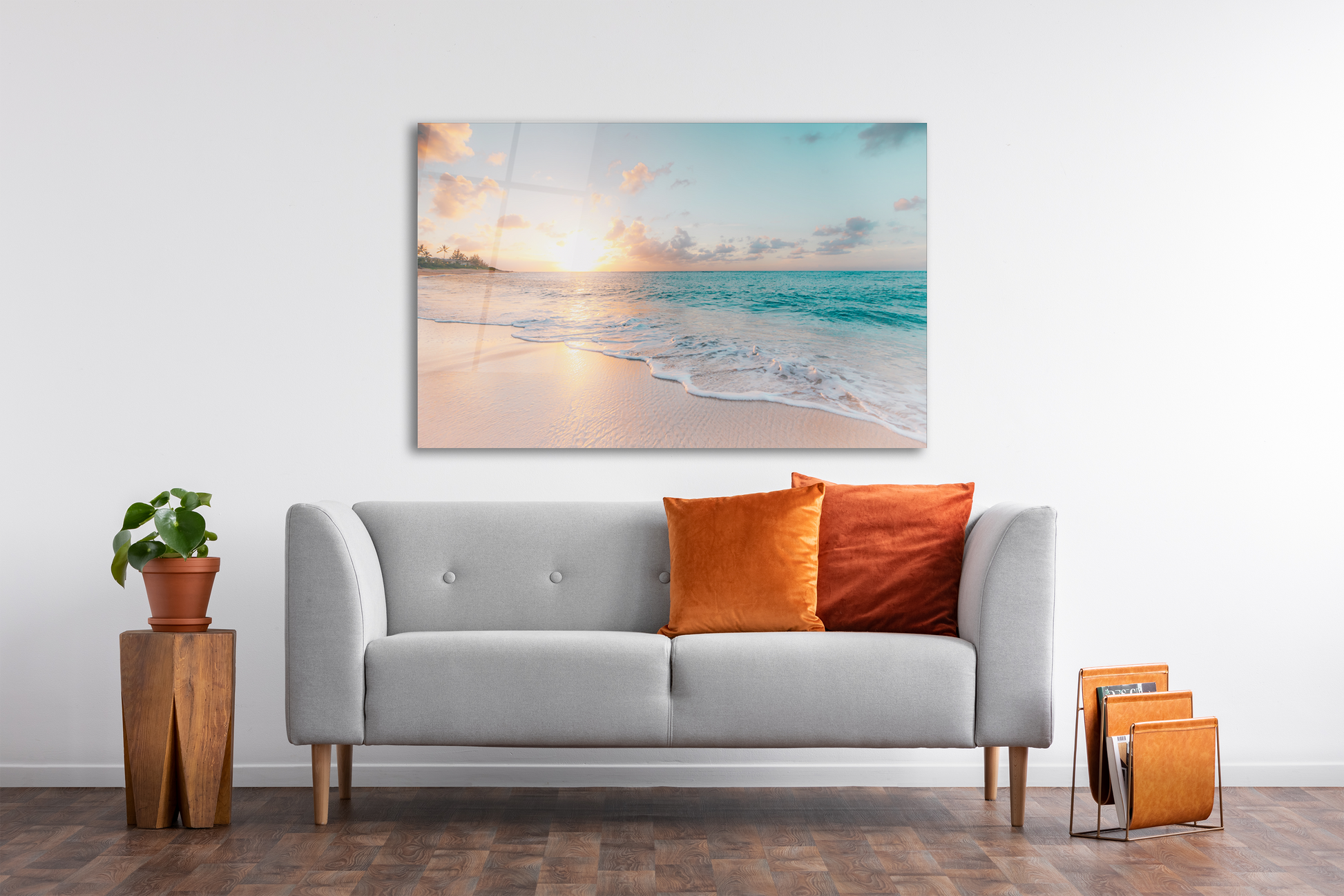Beach wall art on a wall on top of a white couchwith orange pillows a plant pot