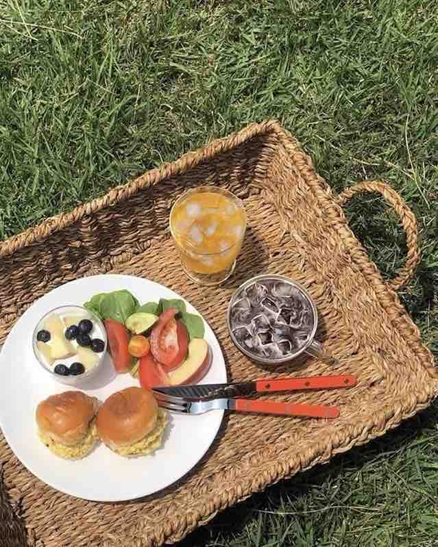 Orange knife and fork with food, fruits in a basket on the grass for a picnic