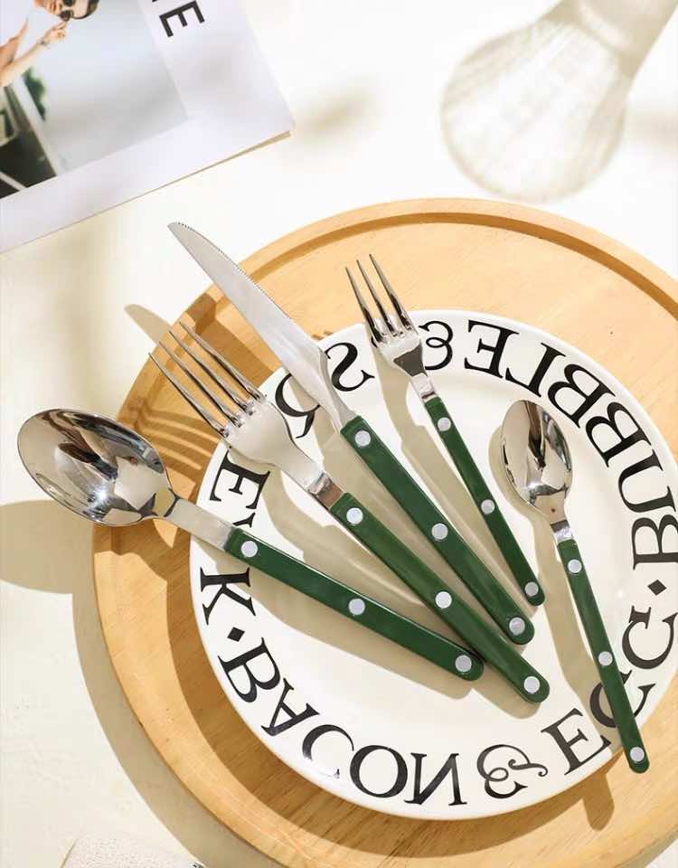 Green silver cutlery with plates and bowl and a bottle on a table