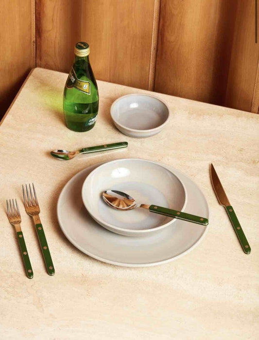 Green silver cutlery with plates and bowl and a bottle on a table