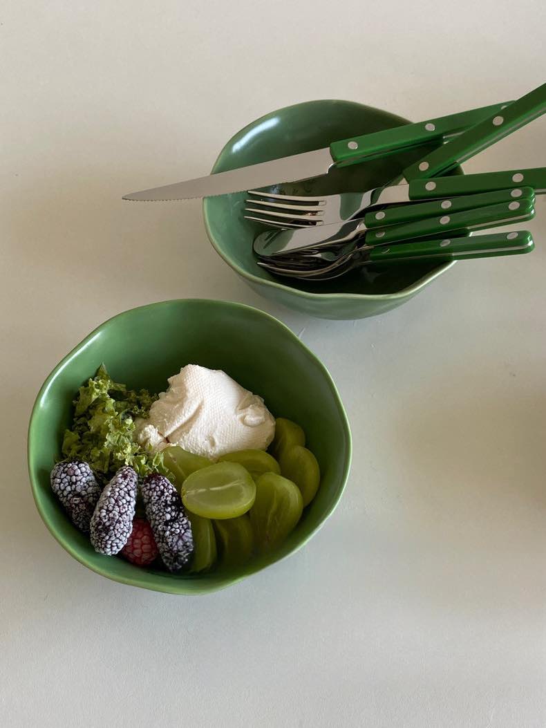 Green silver cutlery in a green bowl on a table with fruits